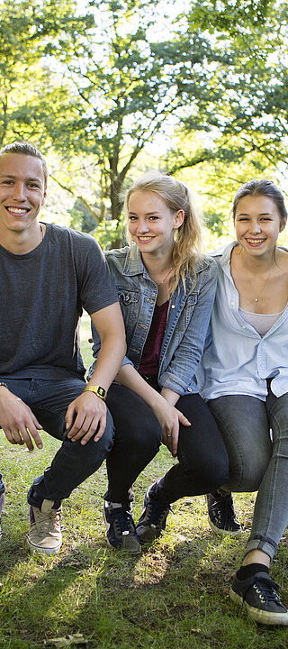 small group of teenagers sitting together on a slackline in a park